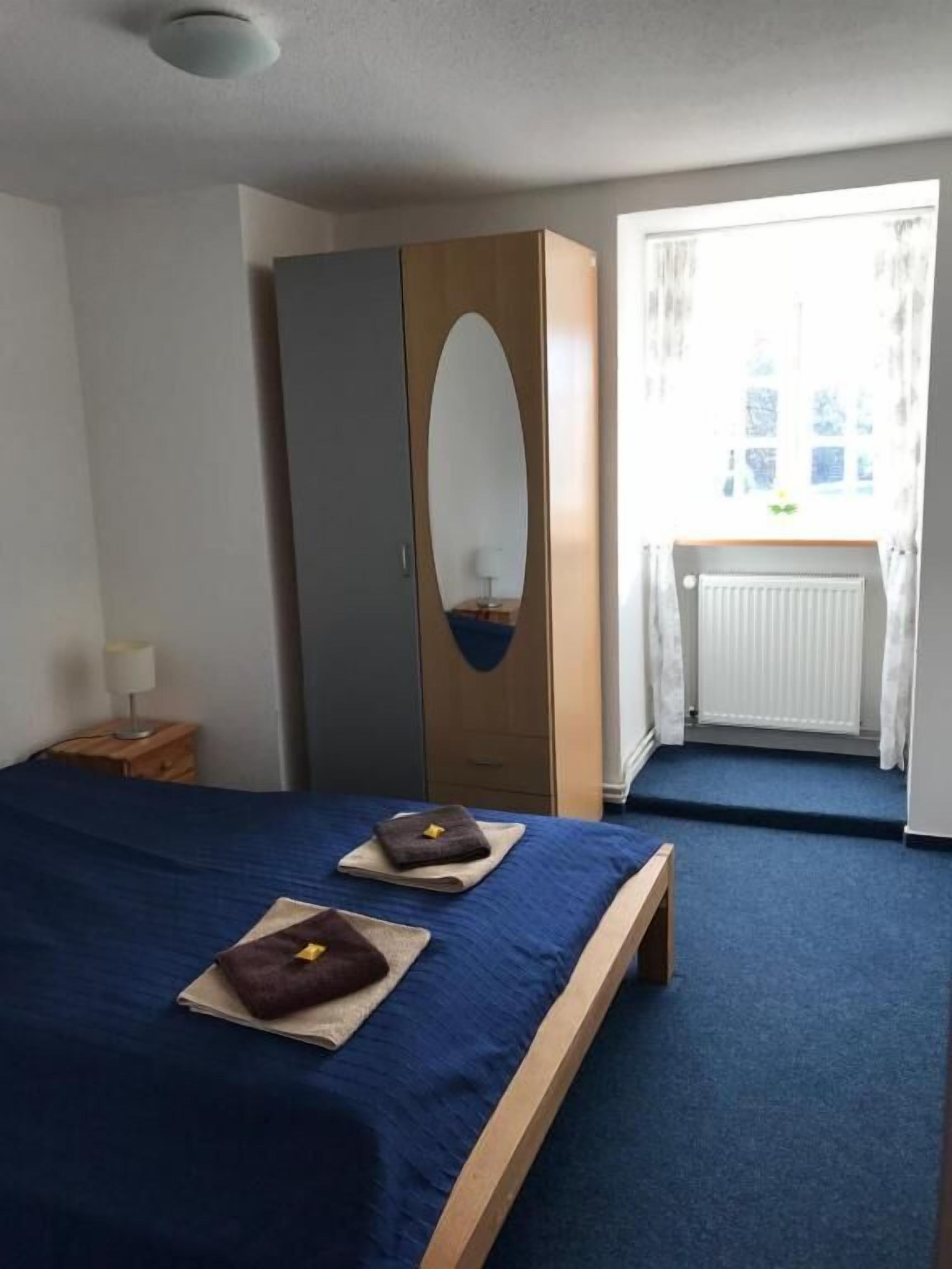 Une chambre à coucher avec un lit, une armoire, une fenêtre avec des rideaux et un radiateur.
