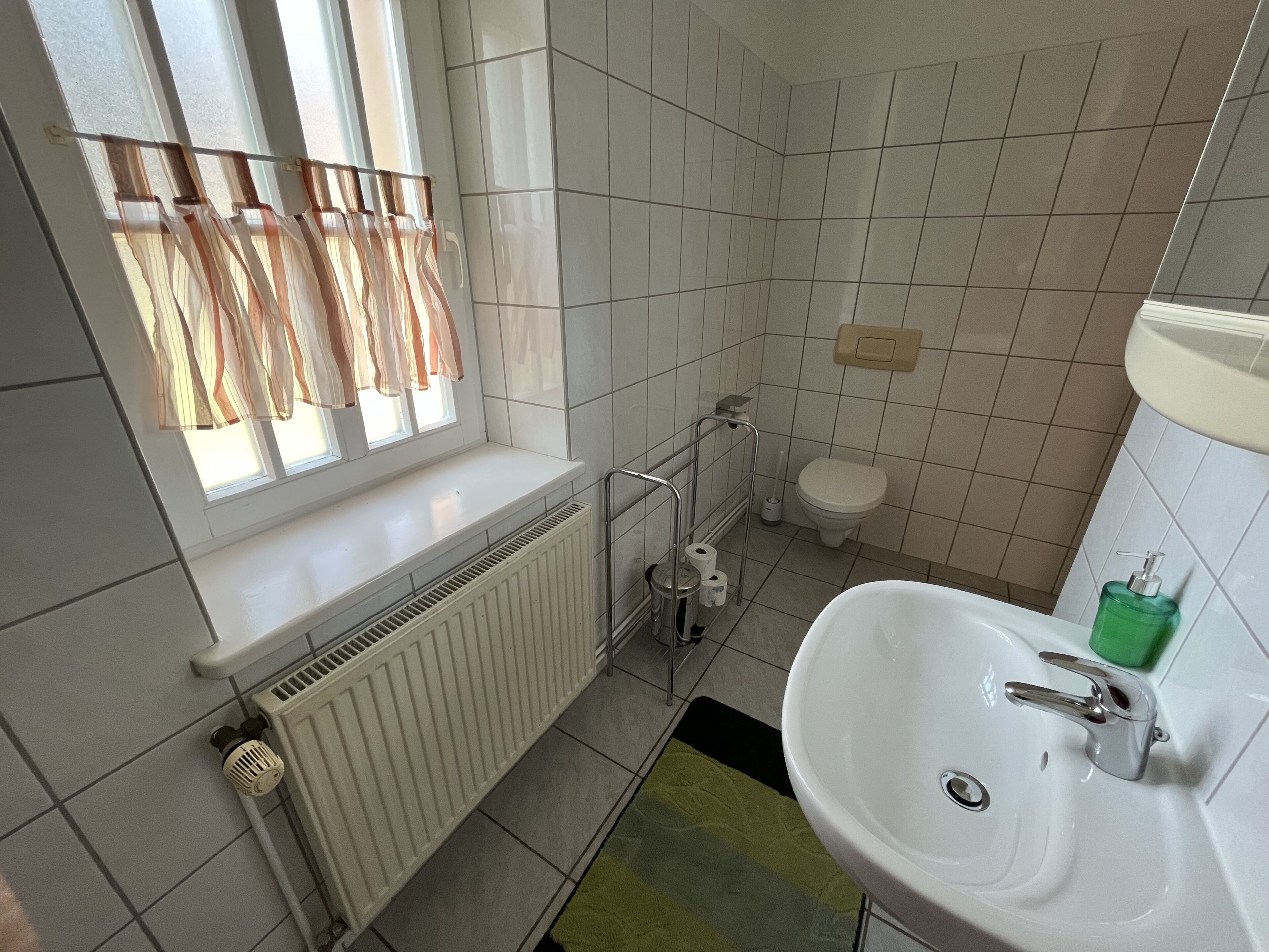 A bathroom with a window, toilet, radiator, and sink.