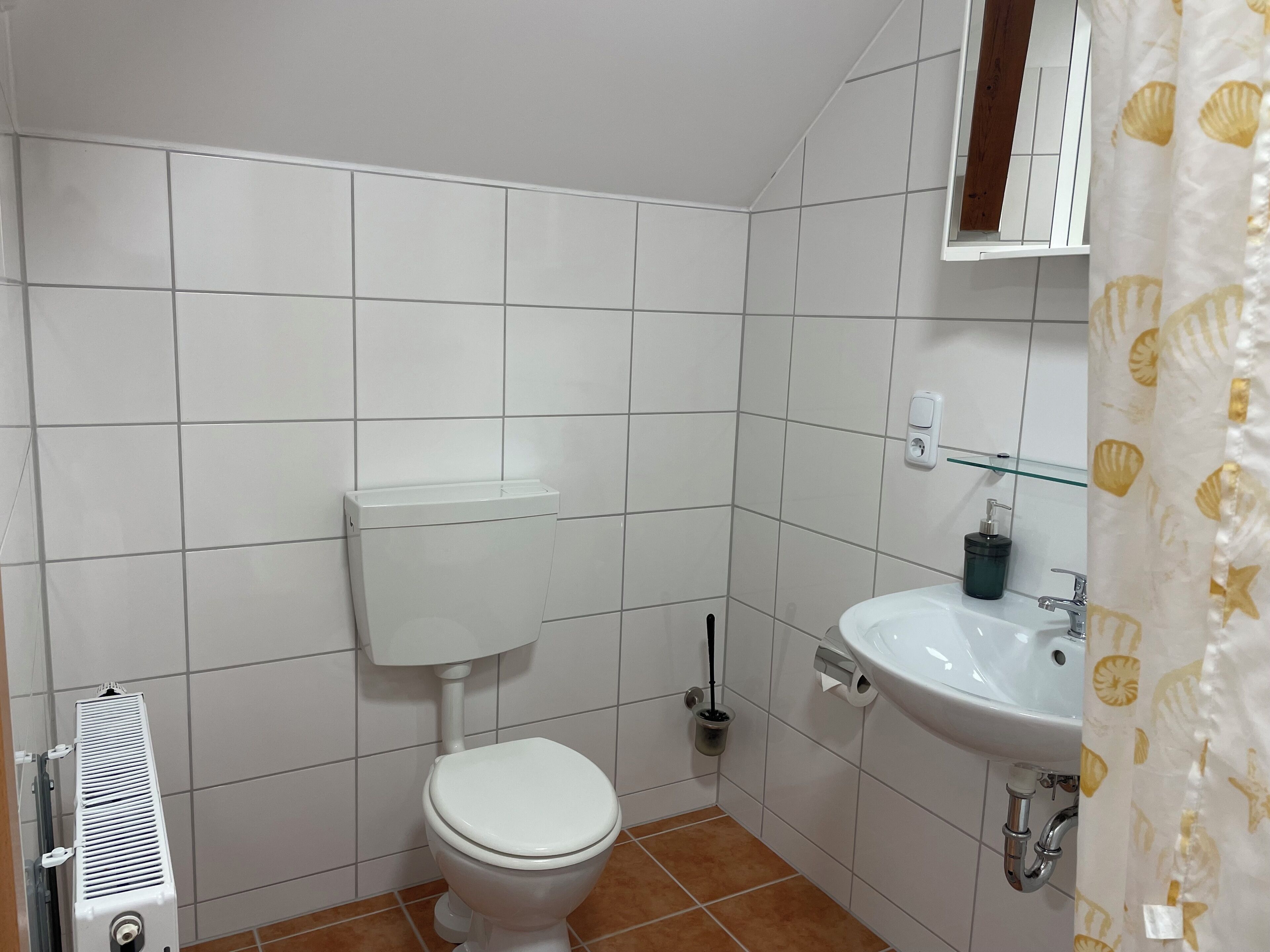 A bathroom with a white toilet, a sink, and a shower curtain with a shell pattern.