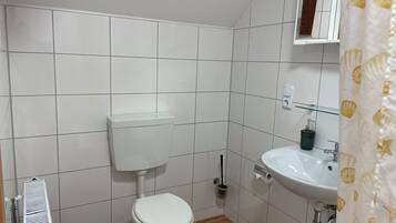 A bathroom with a white toilet, a sink, and a shower curtain with a shell pattern.