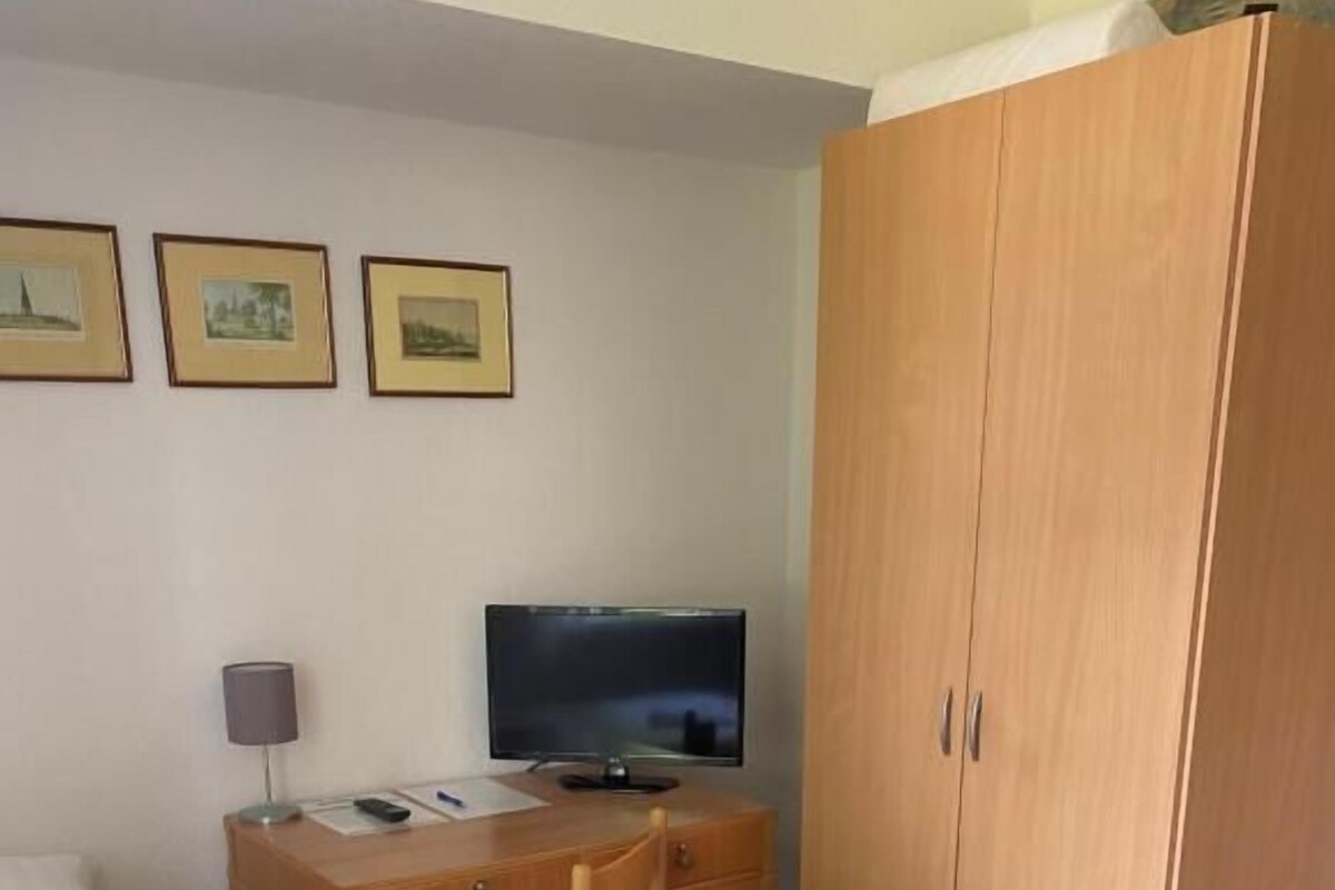 A hotel room with a bed, a desk with a computer, a wardrobe, and framed pictures on the wall.