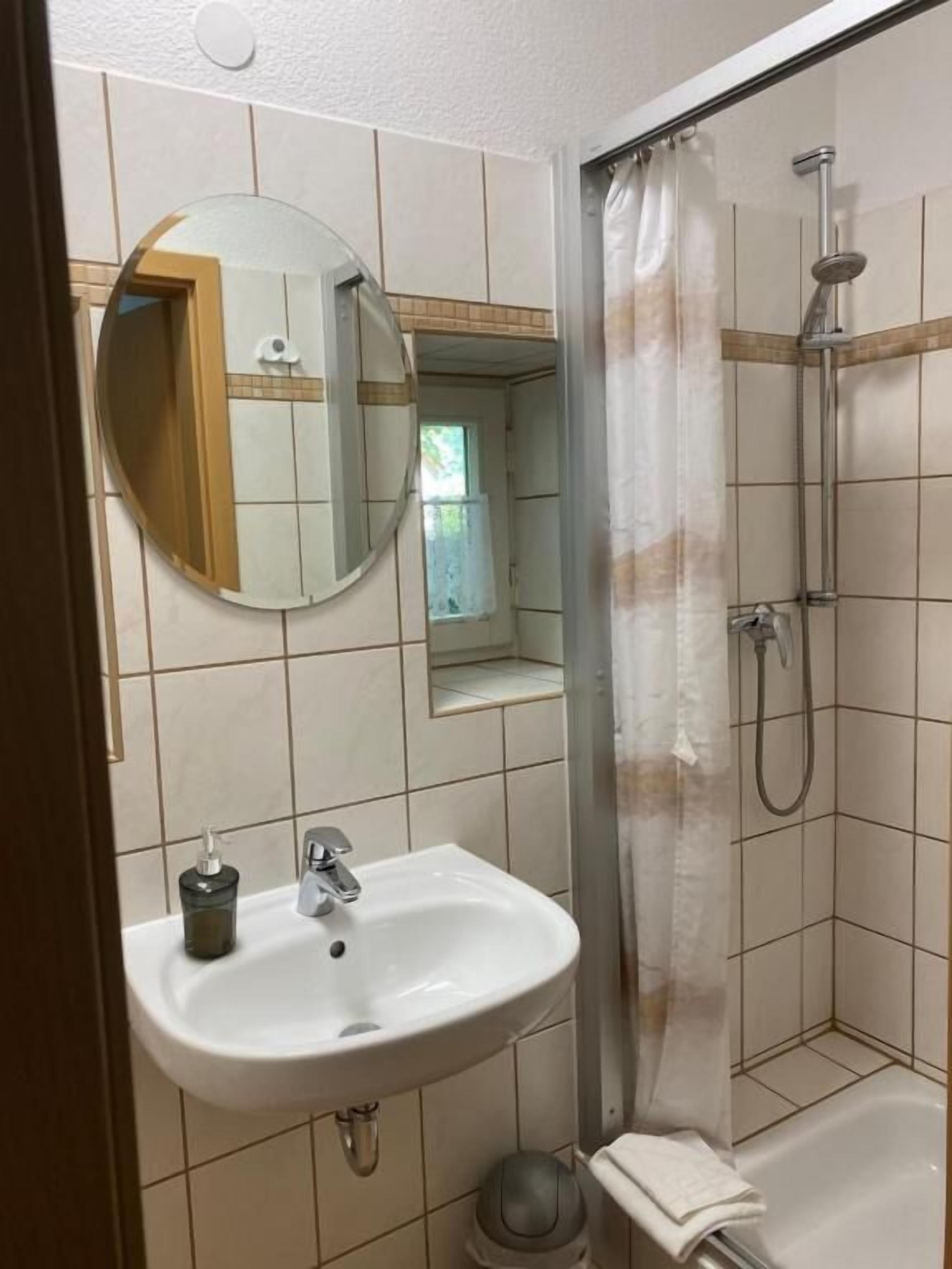 Casa de banho com lavatório, espelho, chuveiro e um porta-toalhas.