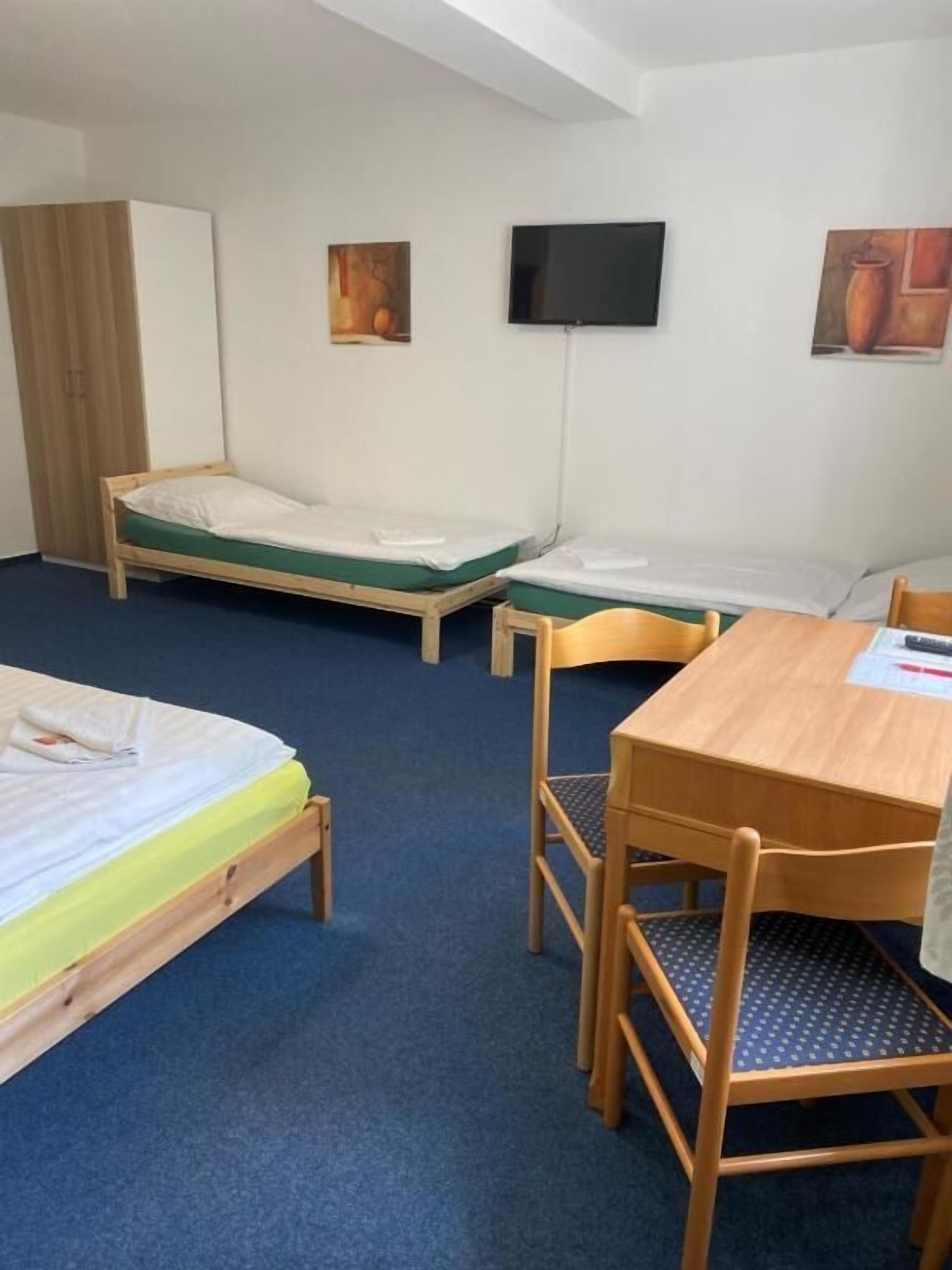 A room with two single beds, a wooden table with chairs, a TV mounted on the wall, and a wardrobe.