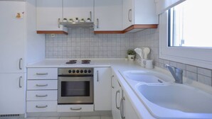 Una cocina con gabinetes blancos, estufa, horno, pileta y ventana.