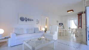 Una sala de estar moderna con un sofá blanco, una mesa de centro de vidrio y un comedor con sillas blancas.