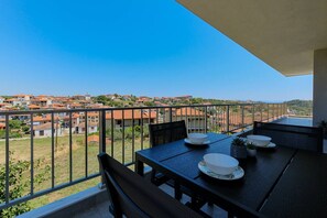 A balcony with a table set for two, overlooking a residential area with red-roofed houses. - DeMar No 5 by RentalsPro - Agios Nikolaos (Chalkidiki)