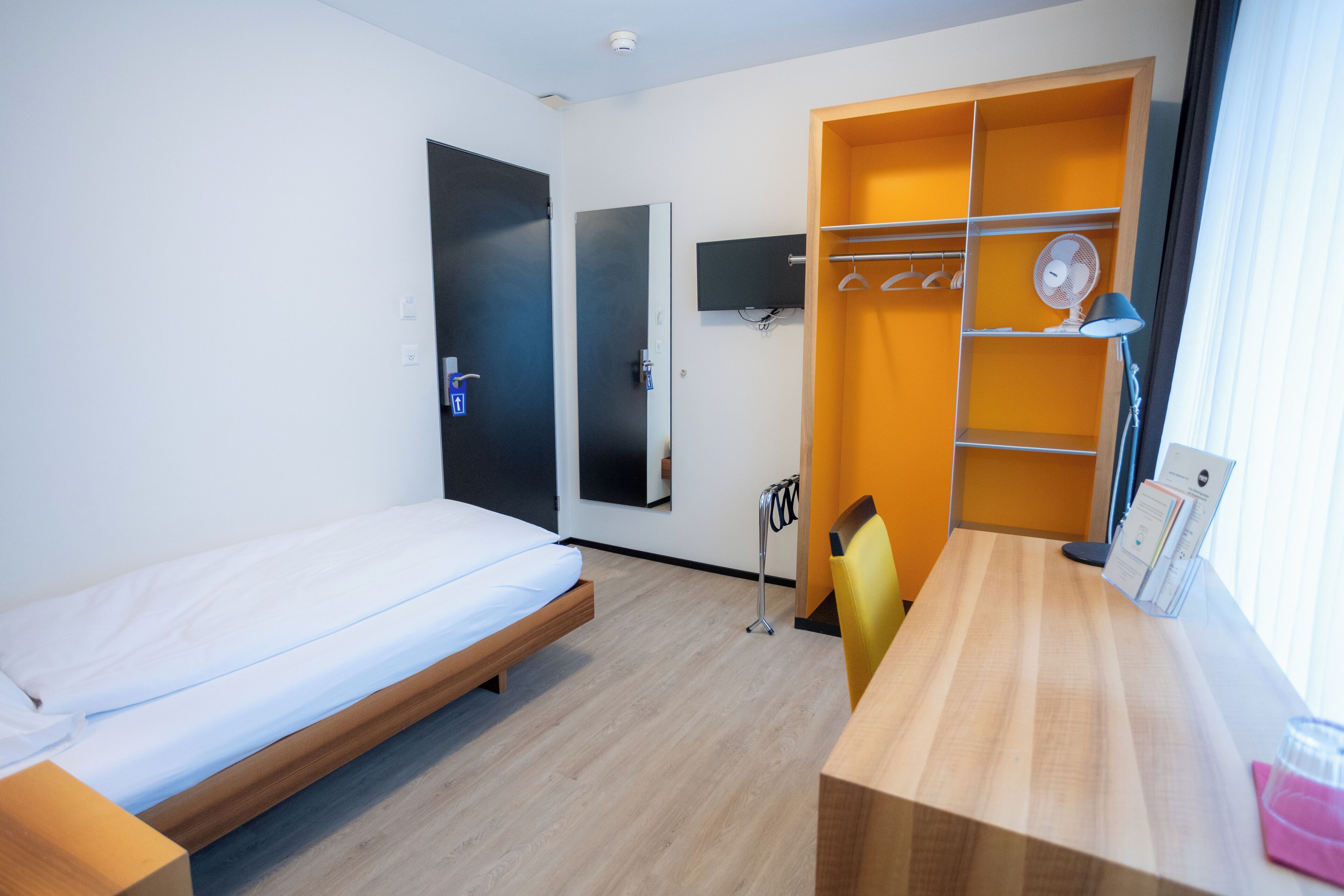 A hotel room with a bed, a desk, a wardrobe, and a window.