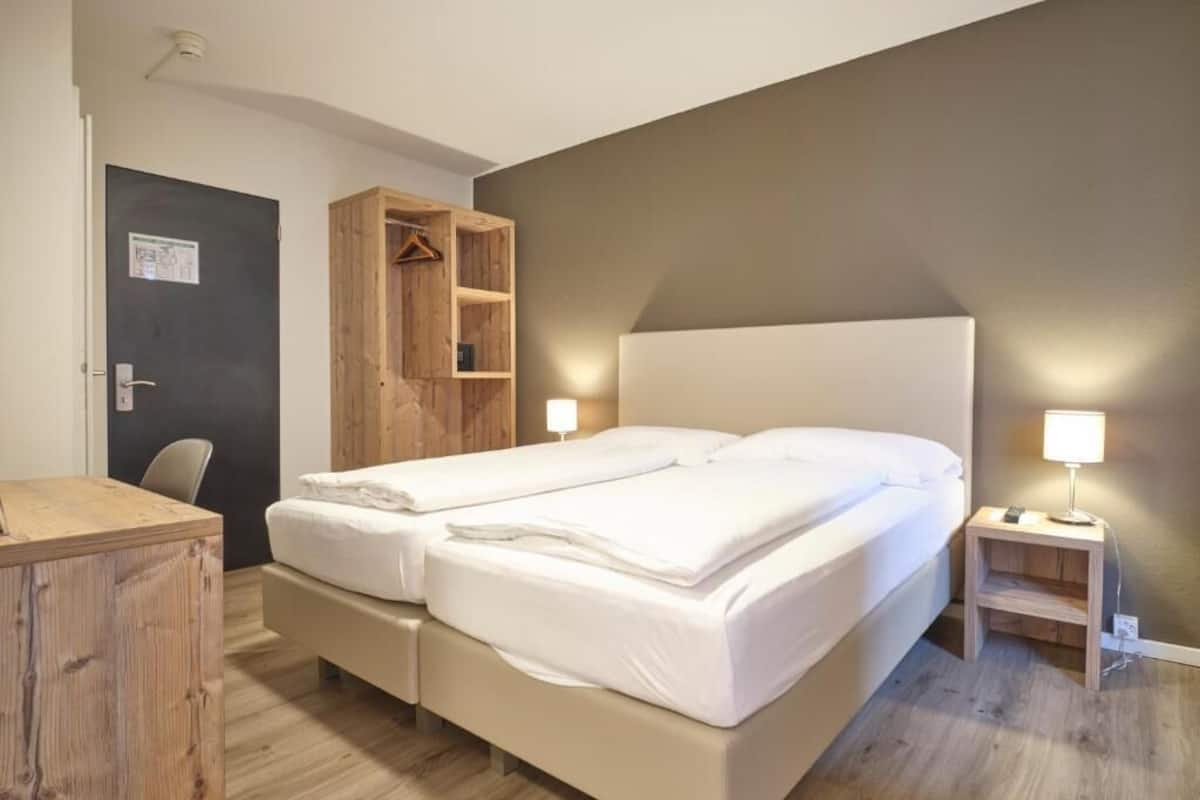 Una cama doble con dos mesitas de noche, un armario de madera y un escritorio.