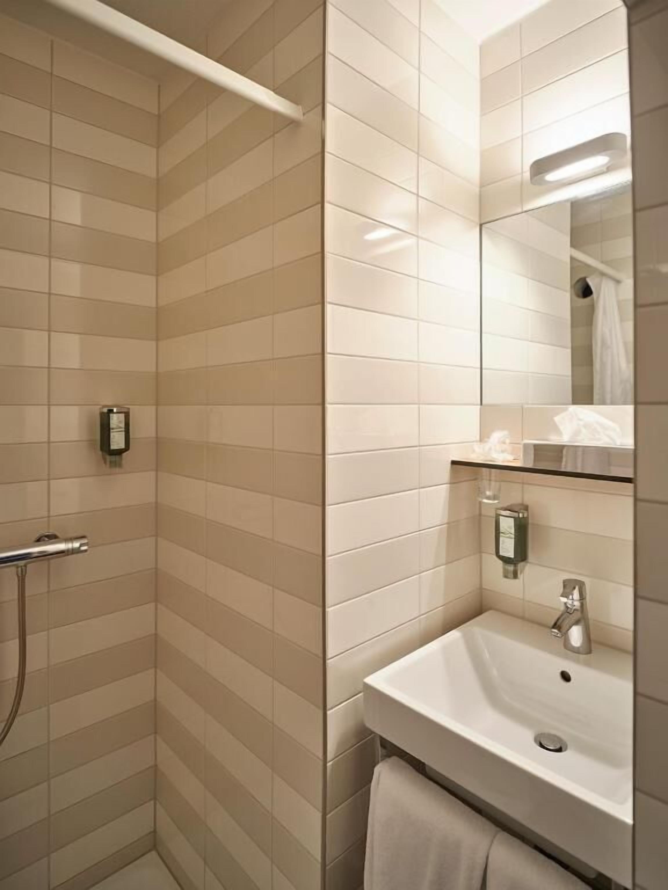 A bathroom with a shower, a sink, a mirror, and a towel rack.