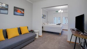 Una habitación de hotel moderna con un sofá gris, una cama, un televisor y obras de arte en las paredes.