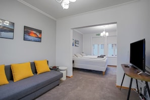 Ein modernes Hotelzimmer mit grauem Sofa, einem Bett, einem Fernseher und Kunstwerken an den Wänden.