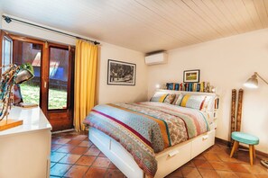 Ein Schlafzimmer mit einem Bett, einem Schreibtisch, einem Stuhl, einem Fenster mit Vorhängen und einer Wand-Klimaanlage.