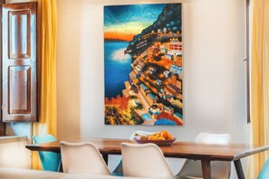 A dining area with a table, chairs, and a painting of a coastal village. - Villa in Massa Lubrense with 3 bedrooms sleeps 6 (Massa Lubrense)