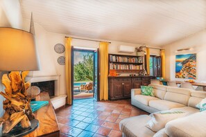 A living room with a fireplace, a sofa, a bookshelf, and a view of the outdoors. - Villa in Massa Lubrense with 3 bedrooms sleeps 6 (Massa Lubrense)