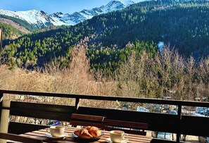 Ein Tisch mit einem Croissant und einer Tasse Kaffee, eine Bank und Blick auf die Berge.