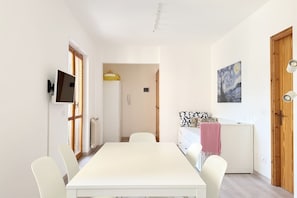 Ein modernes Zimmer mit Esstisch, Stühlen, Fernseher, Kühlschrank und einem Bild an der Wand.