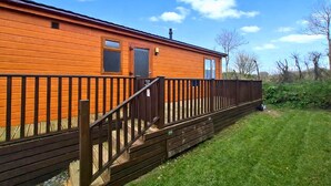 A wooden cabin with a fenced deck and a grassy yard. - Coastal Bella Mere Lodge • 2 Bed • Sleeps 5 (Ilfracombe)