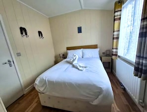 A neatly made bed with a wooden headboard, a bedside table with a lamp, and a window with curtains.