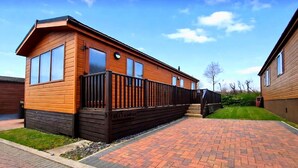 A wooden house with a balcony, a paved driveway, and a well-maintained lawn. - Coastal Bella Mere Lodge • 2 Bed • Sleeps 5 (Ilfracombe)