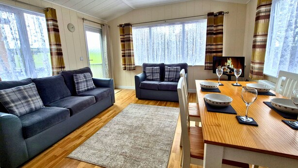 A cozy living room with a sofa, a smaller sofa, a dining table with chairs, and a fireplace. - Coastal Bella Mere Lodge • 2 Bed • Sleeps 5 (Ilfracombe)