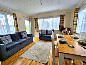 A cozy living room with a sofa, a smaller sofa, a dining table with chairs, and a fireplace.