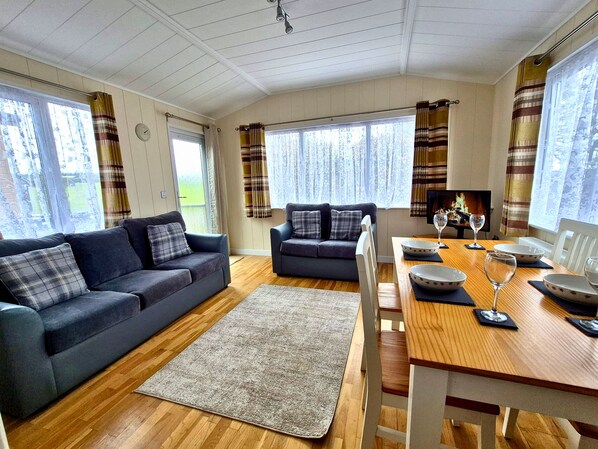 Una sala acogedora con un sofá, un sofá más pequeño, una mesa de comedor con sillas y una chimenea.
