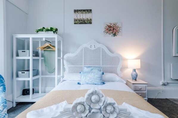 A bedroom with a white bed, a white wardrobe, a bedside table with a lamp, and a wall-mounted mirror. - Chester Heights by Guestz (Chester)