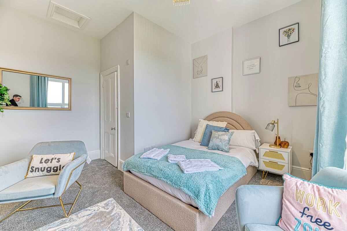 A bedroom with a bed, a chair, a nightstand, a mirror, and wall art.