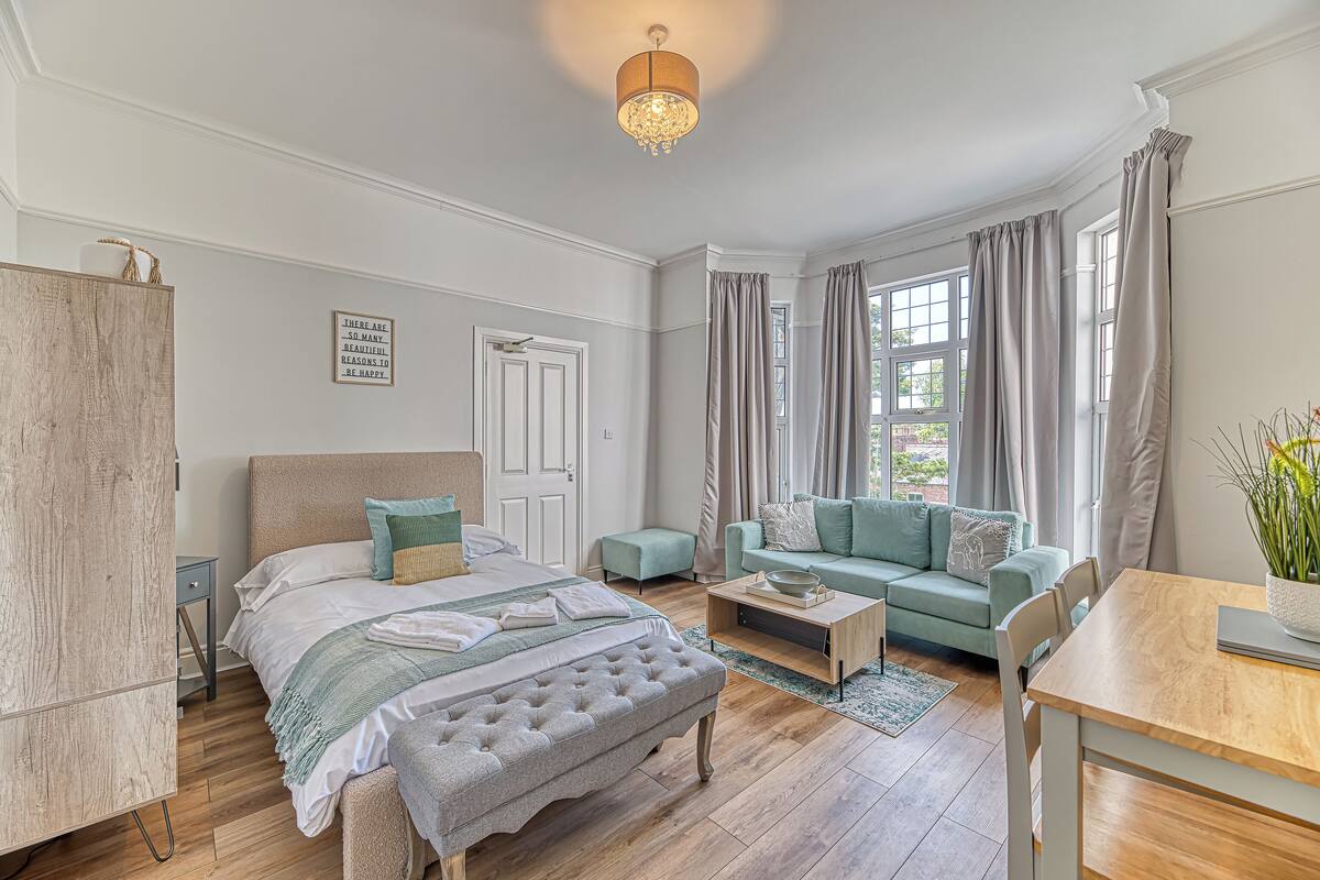 A bedroom with a bed, a wooden wardrobe, a sofa, a coffee table, and a dining table.
