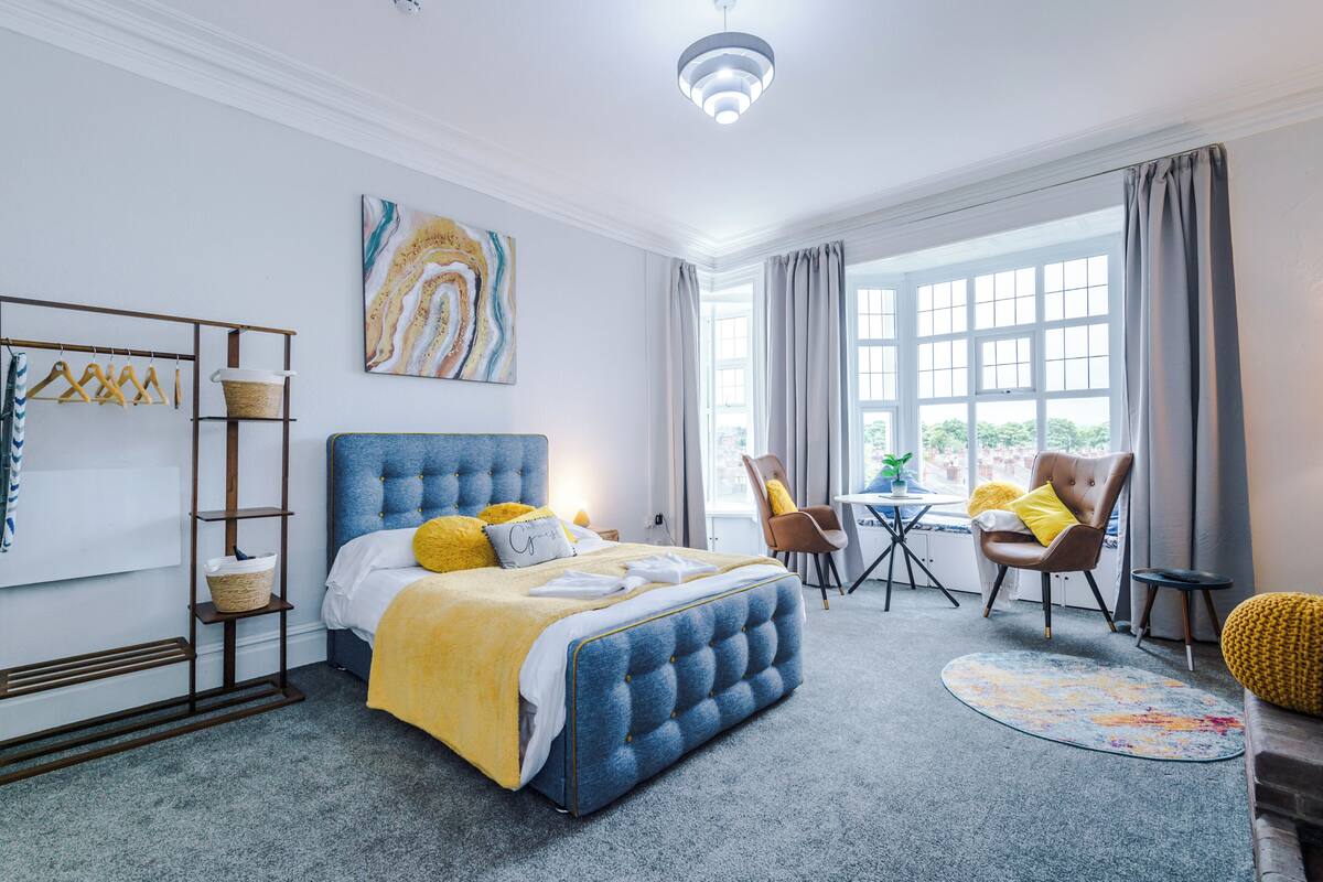 A bedroom with a large bed, a desk, a chair, and a window with curtains.