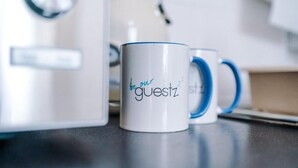 Una taza blanca con el texto 'be our guestz' sobre una encimera.