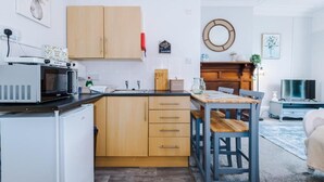 Una cocina compacta con armarios de madera, un microondas, un lavamanos y una zona de comedor con mesa y sillas.