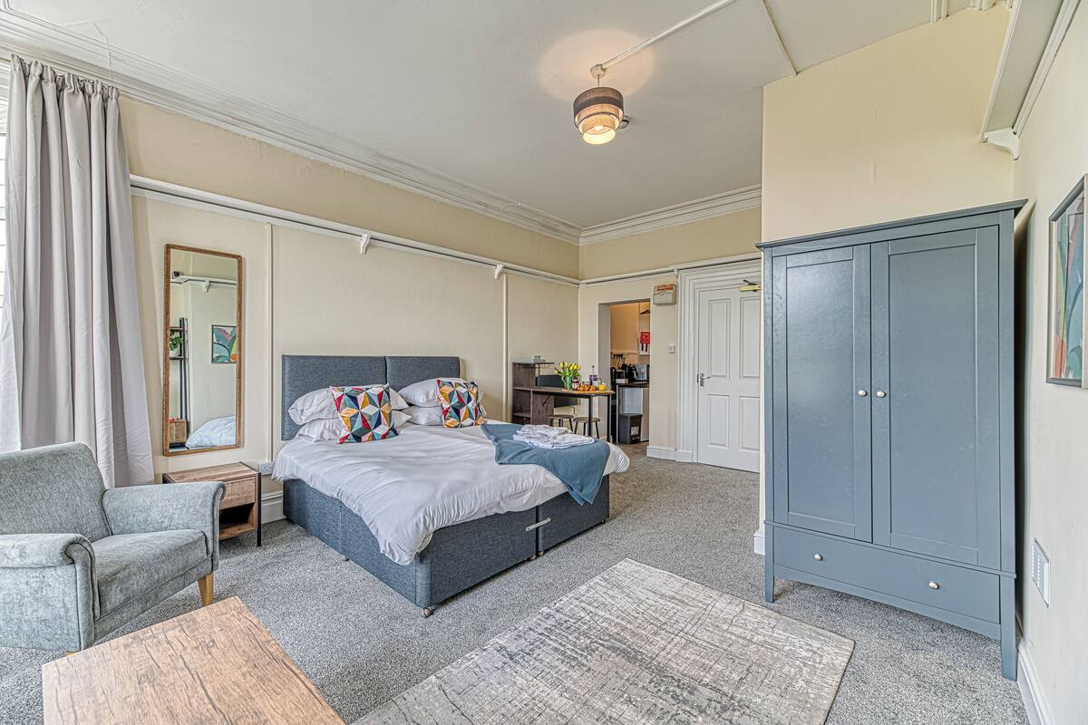 A bedroom with a bed, a chair, a wardrobe, and a desk area.