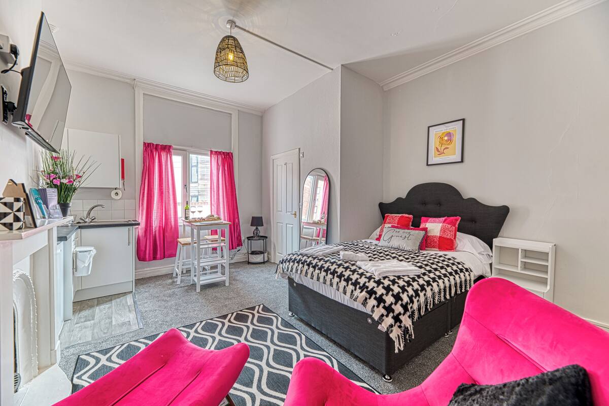 A bedroom with a bed, a desk, a chair, a mirror, and a window with curtains.