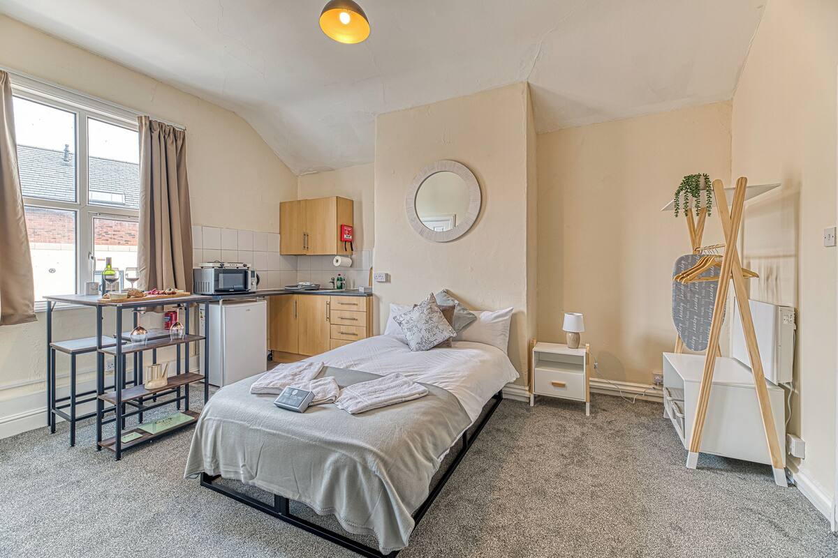 A bedroom with a bed, a desk, a chair, a wardrobe, a mirror, and a plant.