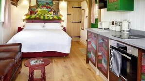 Ein Zimmer mit einem Bett, einem kleinen Tisch, einer Küche mit grünen Schränken und einer Deckenleuchte.