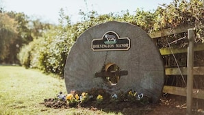 Ein Steinschild mit der Aufschrift 'HORNINGTON MANOR', ein Holzzaun und eine Blumenwiese.