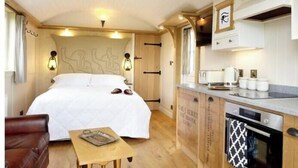 Ein kleines Zimmer mit Bett, Tisch, Küchenzeile und Deckenleuchte.