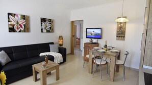 Ein modernes Wohnzimmer mit schwarzem Sofa, Holztisch, Esstisch mit Stühlen, einem Fernseher und Kunstwerken an den Wänden.
