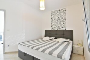 Ein Schlafzimmer mit einem Bett, einem Nachttisch, einer Wandleuchte und einem Fenster.