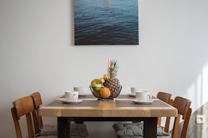 A dining table with a fruit bowl, white cups, and a view of water.