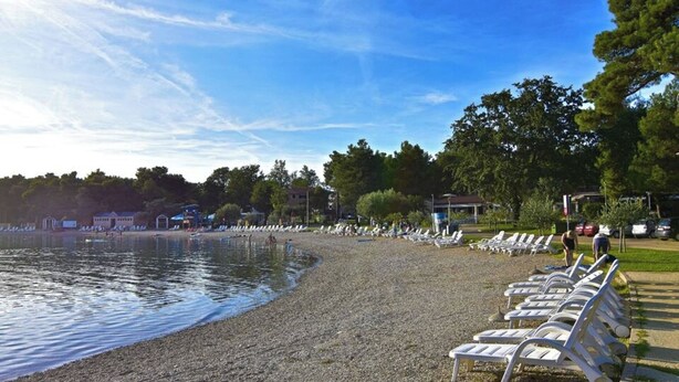 A pebbled beach with lounge chairs, a calm lake, and trees in the background. - Quiet stay with garden view (Umag)