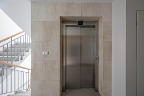 A modern elevator with a metallic finish, a staircase with a wooden handrail, and a light-colored wall. - Modern Apartment | Balcony and Workspace (Warszawa)