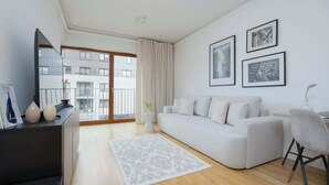 A modern living room with a white sofa, a flat-screen TV, a coffee table, and a large window with a view of a building. - Modern Apartment | Balcony and Workspace (Warszawa)