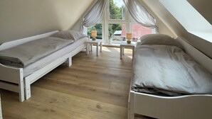 A small, modern attic bedroom with two single beds, a small table, and a window with curtains.