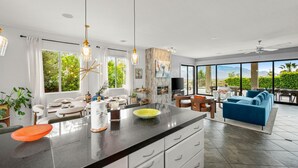 Cozinha moderna com ilha grande, sala de jantar com mobiliário branco e sala de estar com sofá azul.