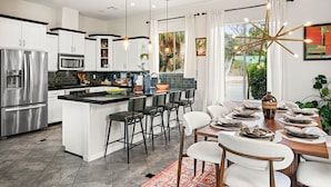 Uma cozinha moderna com eletrodomésticos de aço inoxidável, uma ilha central com banquetas e uma área de jantar com mesa e cadeiras de madeira.