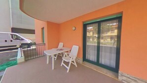 Ein Balkon mit Tisch und Stühlen, eine Glastür zum Verschieben und ein dort abgestellter Wagen.