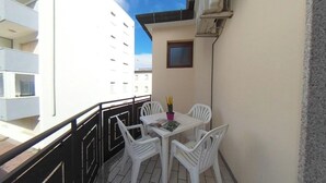 Ein Balkon mit Tisch und Stühlen, ein kleines Fenster und ein Gebäude im Hintergrund.