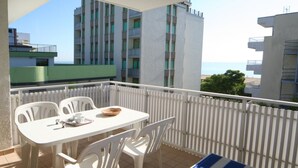 A balcony with a white table and chairs, a blue and white striped tablecloth, and a view of a building with balconies. - Comfortable sea view stay (Lignano Sabbiadoro)